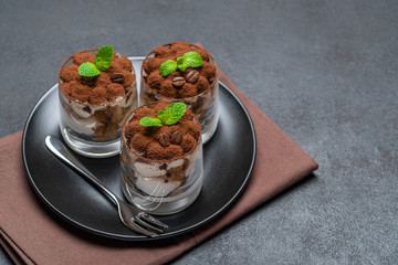 Classic tiramisu dessert in a glass on dark concrete background