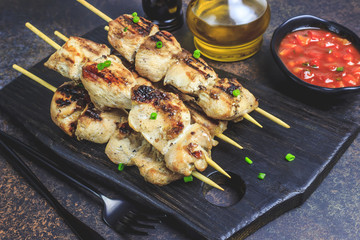 Grilled chicken skewers with green onion and salsa sauce in a cutting board on a dark background. Selective focus