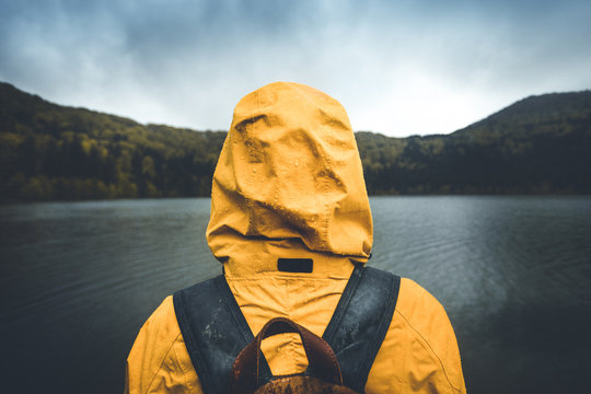 Active outdoors people lifestyle. Rear view of a hiker enjoying rainy weather. Outdoors adventure trek activity, hiker wearing yellow waterproof raincoat sportswear clothes