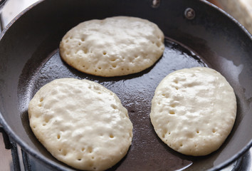 Cooking pancakes on the halfway in a pan with butter as delicious breakfast meal for a happy family