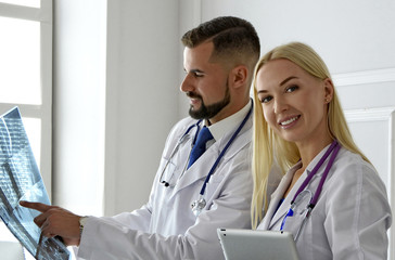 Medical doctors look at MRI spinal scan. Radiologist points at X-Ray. Female and male physicians in white clothes. Co-workers. Practitioners look at x-ray prints. Woman poses.