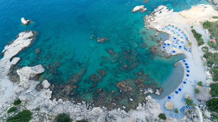 Fototapeta na wymiar Sunny beach lagoon with rocky coastline, Greece. Tourists under umbrella chill relax near clear blue emerald turquoise sea water