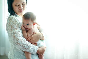 Young mother hugs baby in arms They are both in the window in the bedroom.