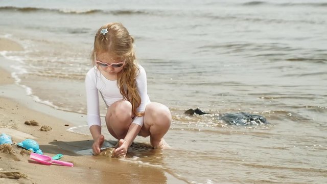 Girl child plays with sand on the beach using molds figurines. Sunny summer day. vacation