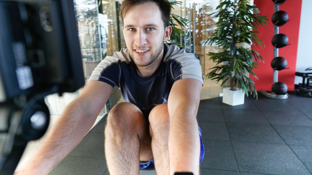 Fitness smiling young man using rowing machine in the gym