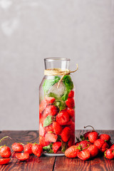 Bottle of Infused Water with Fresh Strawberry and Basil Leaves.Scattered Berries on Wooden Table. Vertical Orientation and Copy Space.