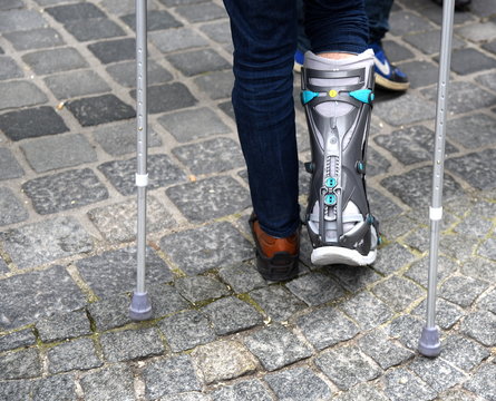 Mit Unterschenkelorthese und Kr&uuml;cken eine Stra&szlig;e entlang gehende Person