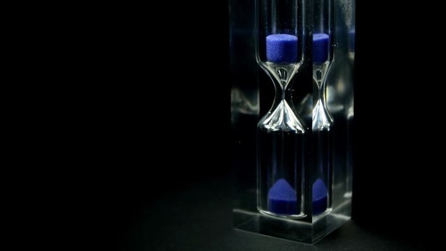 Hourglass, sandglass close-up on a dark background. Sand texture, falling sand. Full-HD 1920 X 1080.