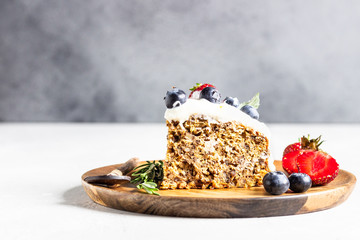 Wholegrain cake with zucchini, carrot and walnuts decorated with whipped cream, strawberries, blueberries, mint and rosemary on a wooden plate. 