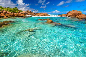 Turquoise sea of natural pool in La Digue. Clear calm waters of swimming pools at Anse Cocos near Grand Anse and Petite Anse protected by rock formations. Peaceful wallpaper of tropical Seychelles.