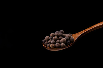 Pepper allspice on wooden spoon over black background. Jamaican bell pepper.