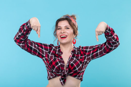 Cute positive young woman in a plaid shirt and bandage poses on a blue background and shows her fingers down. Concept of subscription link below.