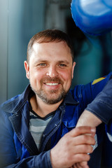 A man with a beard in working clothes smiles a snow-white smile at the workplace in the boiler...