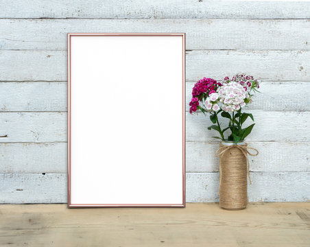 Rose Gold Vertical A4 Frame mocap near a bouquet of sweet-william stands on a wooden table on a painted white wooden background. Rustic style, simple beauty. 3 render