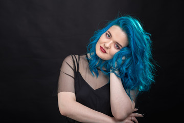 People and fashion concept - Young and attractive woman with black lipstick and blue hair posing over black background