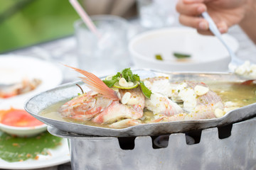 Steamed fish in lemon sauce on a stove with hot fire and ready ro served. The famous Thai food menu with sour and delicious taste. Close up and blur.