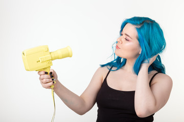 People, hobby and fashion concept - Beautiful girl with blue hair hold yellow retro camera on white background