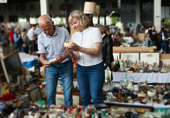 Fototapeta na wymiar Glad man and woman choosing interesting souvenirs at traditional flea market