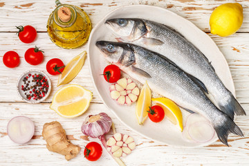 Two raw fresh sea bass ready for baking with tomatoes, lemon, red onion, garlic, ginger, parsley and spices. Prepare a tasty and healthy lunch or dinner in a Mediterranean style. Selective focus
