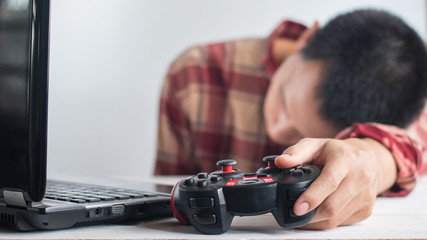 Young Men wear red Scott pattern shirt sleeping Hand holding Joystick gamepad and laptop on white wood desk