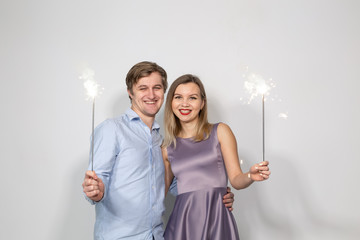 Holidays, party and celebrations concept - young couple with sparklers on white background