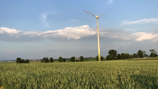 Timelaps of a windmill rotating around its own axis on green meadow with cloudy sky in the background.