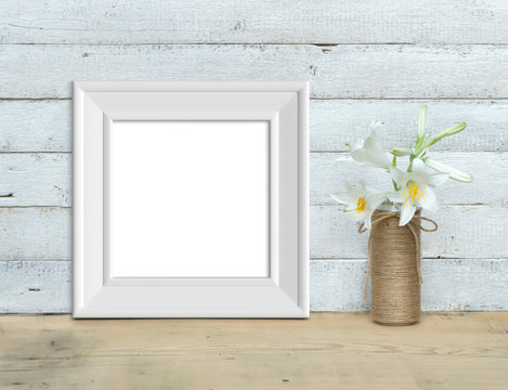 Square Vintage White Wooden Frame mockup near a bouquet of lilies stands on a wooden table on a painted white wooden background. Rustic style, simple beauty. 3d render.