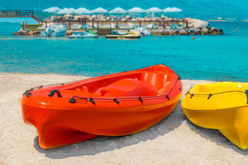 Red and yellow kayaks on white sand on the beach of Cyprus against the backdrop of the sea and umbrellas on the coast
