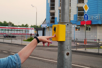 The hand of a girl with a clock presses the button of the pedestrian crossing. A hand sign indicates a button. The button is lit in red, modern electronic pedestrian crossing.