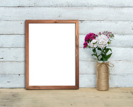 Vertical A4 Old Wooden Frame mockup near a bouquet of sweet-william  stands on a wooden table on a painted white wooden background. Rustic style, simple beauty. 3d render.