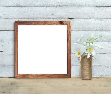 Square Old Wooden Frame mockup near a bouquet of lilies stands on a wooden table on a painted white wooden background. Rustic style, simple beauty. 3d render.