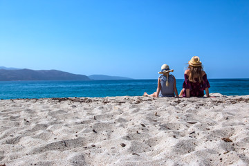 zwei Mädchen sitzen am Strand und schauen auf das Meer