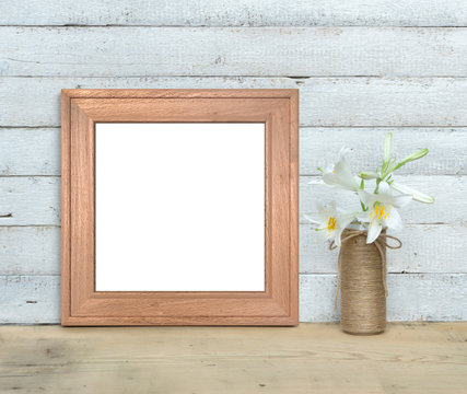 Square Old Wooden Frame mockup near a bouquet of lilies stands on a wooden table on a painted white wooden background. Rustic style, simple beauty. 3d render.