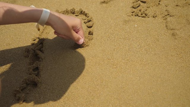 Girl drawing heart symbol on sand beach.