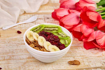 Bowl with Granola, banana, kiwi, berry with pink tulip flowers