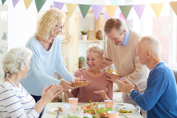 Happy excited beautiful lady with short hair sitting at table and thinking about wish before blowing candles