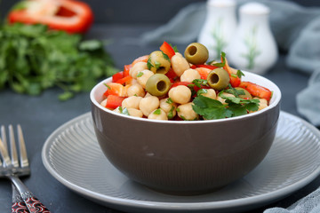 Healthy salad of chickpea, green olives, pepper and parsley, is located on a dark background