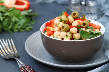 Healthy salad of chickpea, green olives, pepper and parsley, is located on a dark background