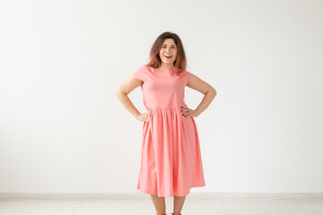 Beautiful young cheerful woman in a long peach dress posing on a white wall. Concept of stylish young woman. Copy space