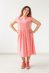 Beautiful young cheerful woman in a bright pink dress posing on the background of a white wall. The concept of stylish feminine images.