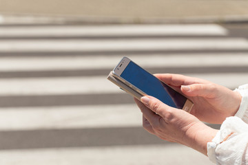 A woman at a pedestrian crossing looking at the smartphone