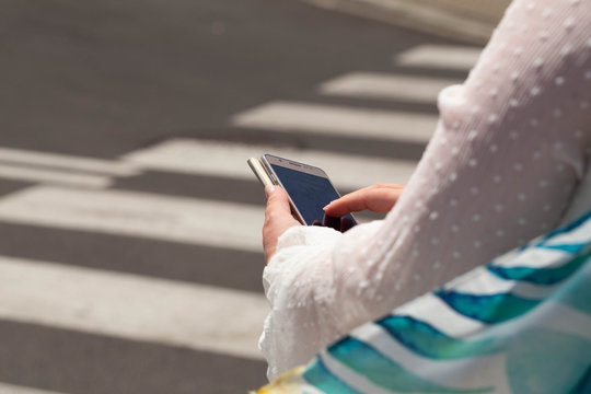 The woman, straring at the phone, crosses the streets / concept