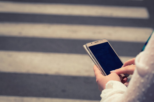 The woman, straring at the phone, crosses the streets / concept