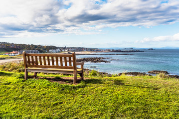 Fototapeta na wymiar Empty wooden bench overlooking the coastal town of North Berwick on a sunny autumn day. Scotland, UK