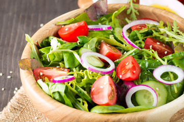 Fresh healthy vegetable salad made of cherry tomato, ruccola, arugula, feta, olives, cucumbers, onion and spices. Greek, Caesar salad in a bowl on wooden background. Healthy organic food concept.