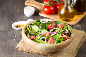Fresh healthy vegetable salad made of cherry tomato, ruccola, arugula, feta, olives, cucumbers, onion and spices. Greek, Caesar salad in a bowl on wooden background. Healthy organic food concept.