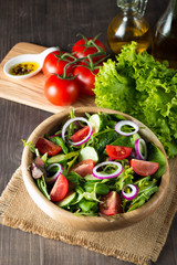 Fresh healthy vegetable salad made of cherry tomato, ruccola, arugula, feta, olives, cucumbers, onion and spices. Greek, Caesar salad in a bowl on wooden background. Healthy organic food concept.