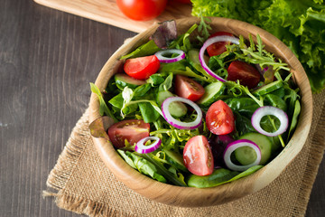 Fresh healthy vegetable salad made of cherry tomato, ruccola, arugula, feta, olives, cucumbers, onion and spices. Greek, Caesar salad in a bowl on wooden background. Healthy organic food concept.
