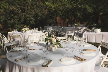 Wedding table setting decorated with fresh flowers in a brass vase. Wedding floristry. Banquet table for guests outdoors with a view of green nature. Bouquet with roses, eustoma and eucalyptus leaves