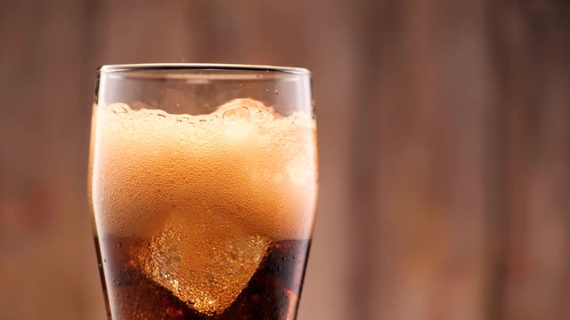 Cola pouring in tall glass thish ice cubes ib slow motion. A lot of bubbles and sparkling.